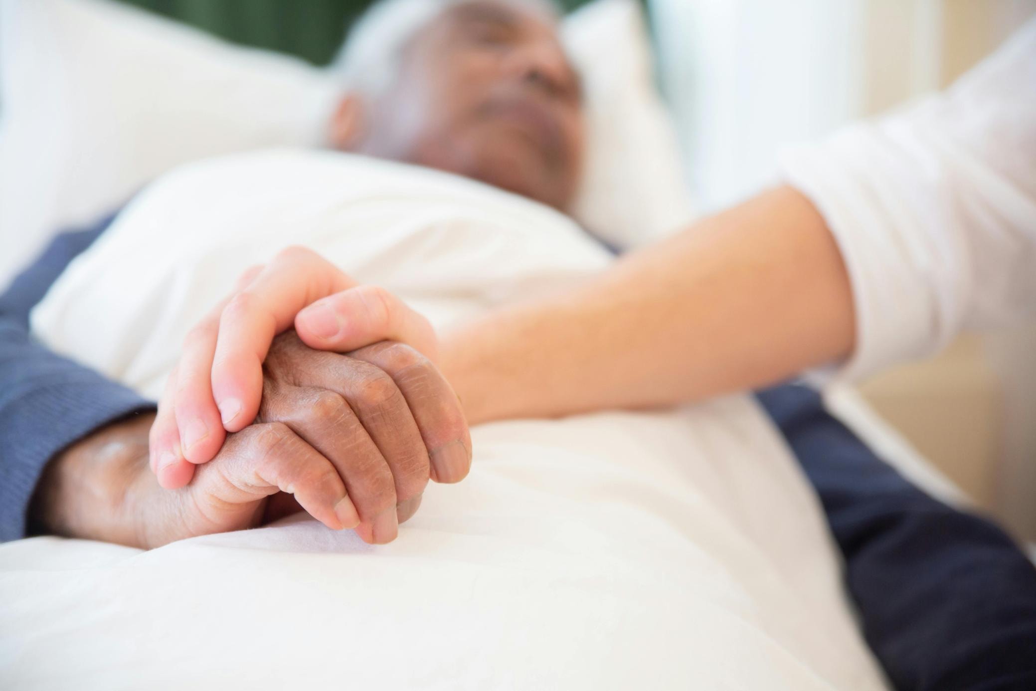 resident-in-bed-with-family-member-holding-hand