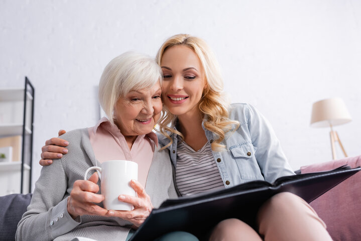 older woman looking at a photo album with family on a visit to a care home
