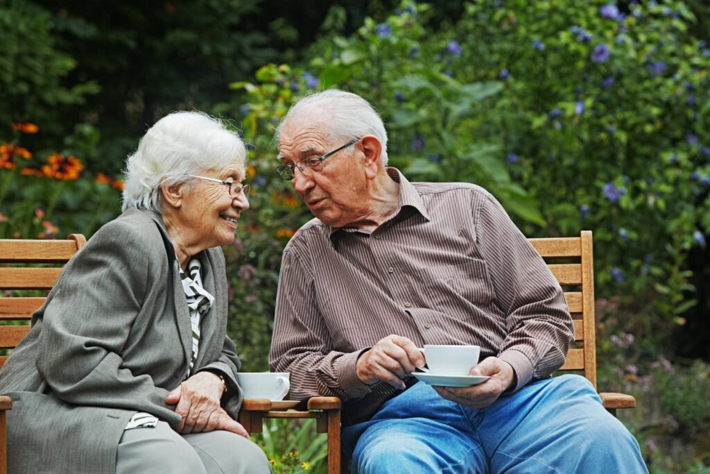 man and a women smiling together in a garden on a wooden bench